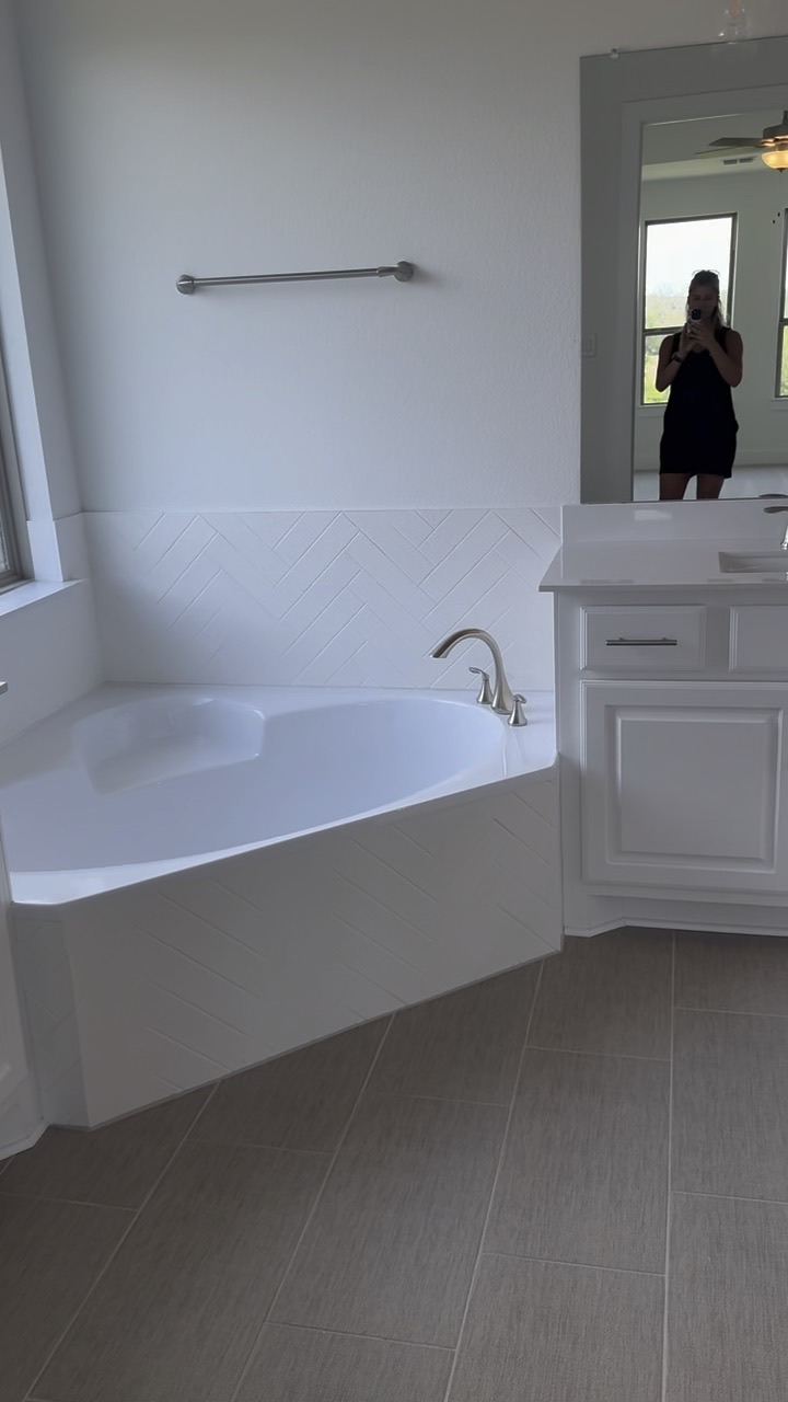 Primary bathroom with a corner soaking tub, white herringbone tile, and a vanity