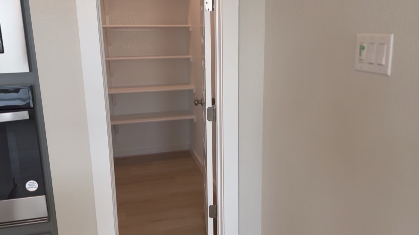 Open door to a walk-in pantry with tall white shelving
